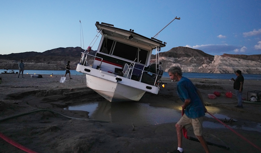 Craig Miller hauls a hose while trying to free his stranded houseboat at the Lake Mead National Recreation Area, Thursday, June 23, 2022, near Boulder City, Nev. Miller had been living on the stranded boat for over two weeks after engine trouble and falling lake levels left the boat above the water level.