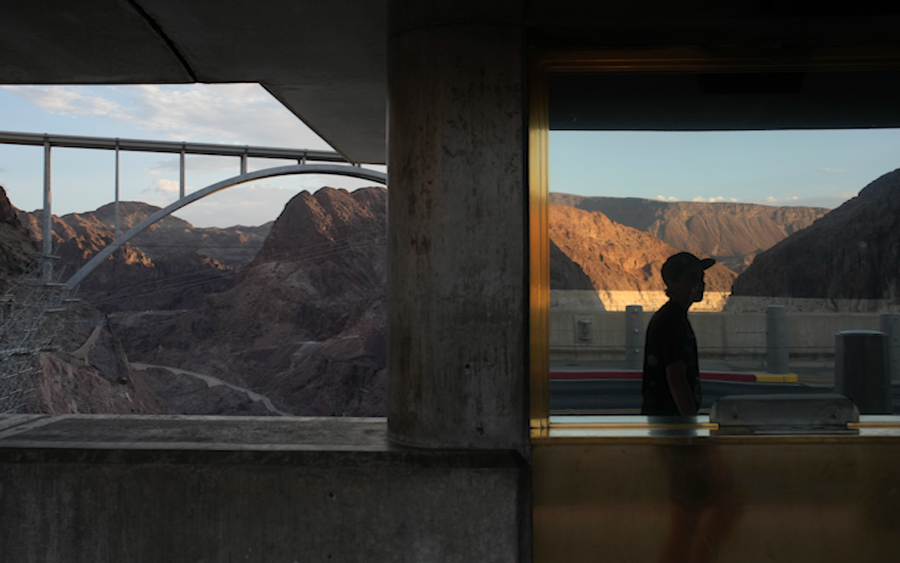 A person is reflected in a window as they walk across Hoover Dam at Lake Mead, Sunday, June 26, 2022, near Boulder City, Nev. The bathtub ring of light minerals around Lake Mead shows the high water mark of the reservoir which has fallen to record lows.